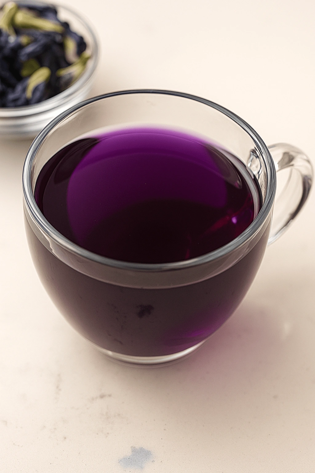 Glass cup of purple Brazilian Mounjaro tea with dried butterfly pea flowers in background.